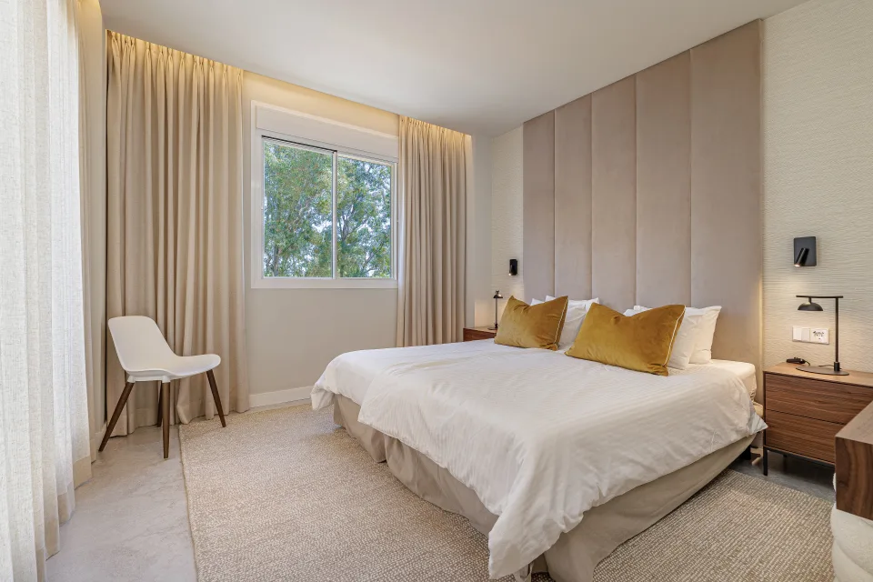 Fotografía de alquiler vacacional de un dormitorio luminoso con cama doble, cabezal acolchado y ventanales grandes en Nueva Andalucía