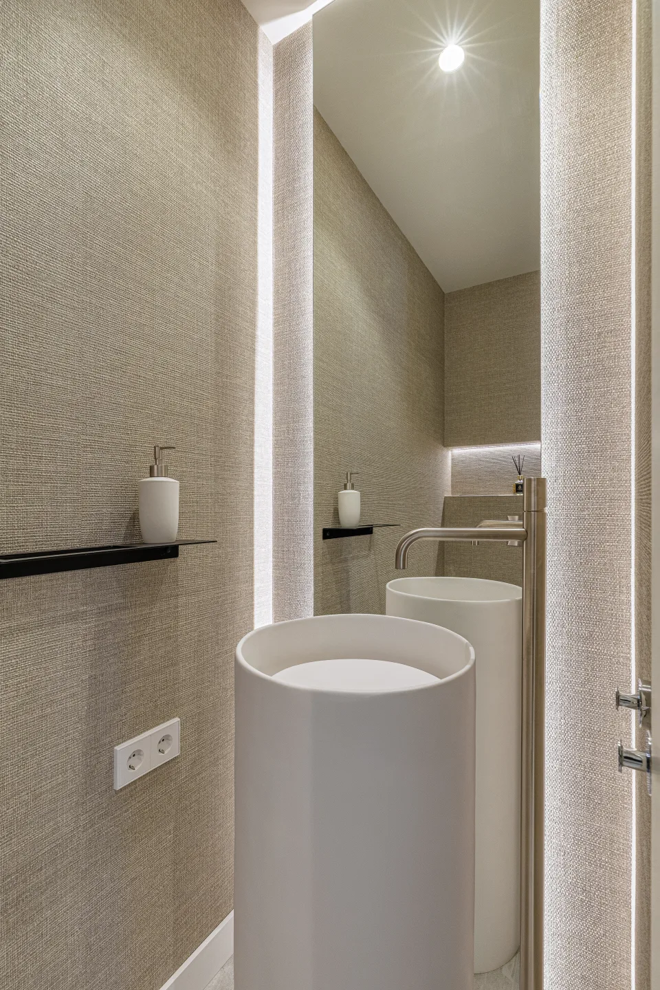 Fotografía de alquiler vacacional de un lavabo moderno blanco en un baño elegante con paredes texturizadas y luz indirecta en Nueva Andalucía | Penthouse en Urb. Fuente Aloha