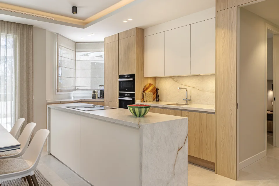 Vacation rental photograph of a modern kitchen with light wood finishes, marble countertop and integrated appliances in Nueva Andalucía