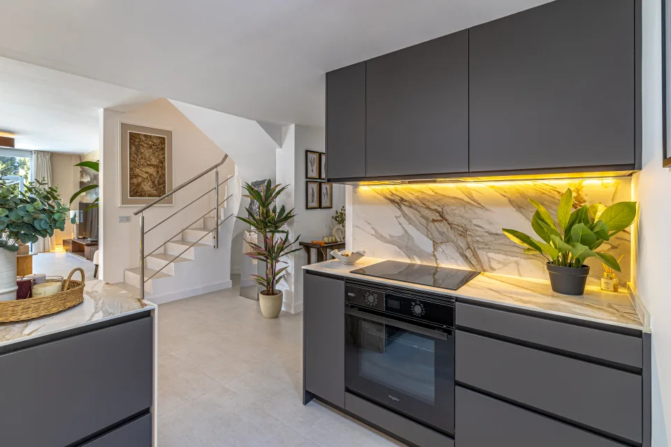 Fotografía de interiorismo y arquitectura de una cocina moderna con acabados en mármol, muebles oscuros y iluminación cálida en Cala de Mijas