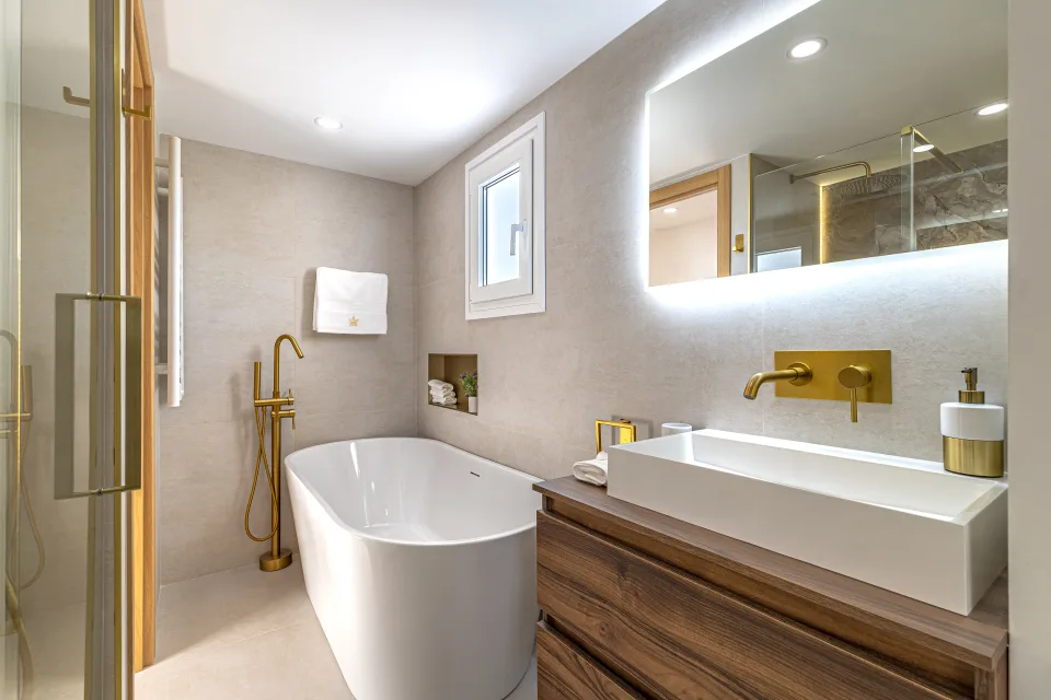 Fotografía de interiorismo y arquitectura de un baño moderno con bañera exenta, grifería dorada y mueble de lavabo de madera en Cala de Mijas