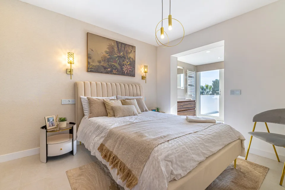 Fotografía de interiorismo y arquitectura de un dormitorio luminoso con cama tapizada, iluminación cálida y decoración moderna en Cala de Mijas