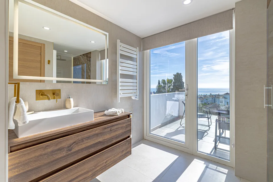 Fotografía de interiorismo y arquitectura de un baño luminoso con lavabo sobre mueble de madera, espejo amplio en Cala de Mijas
