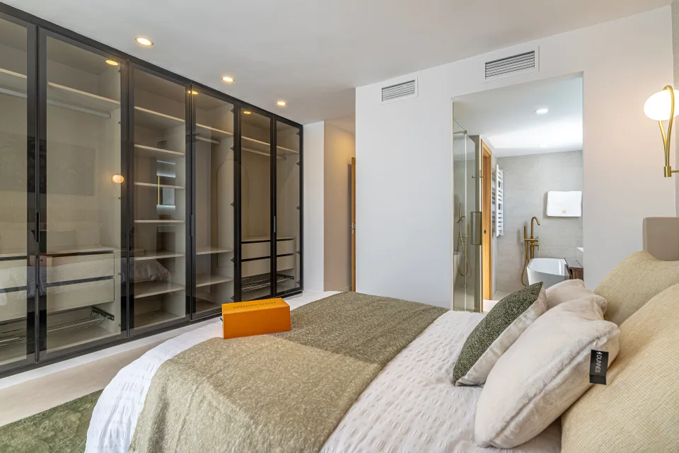 Interior design and architecture photograph of a bright bedroom with neutral-toned bedding, glass wardrobe and minimalist decor in Cala de Mijas