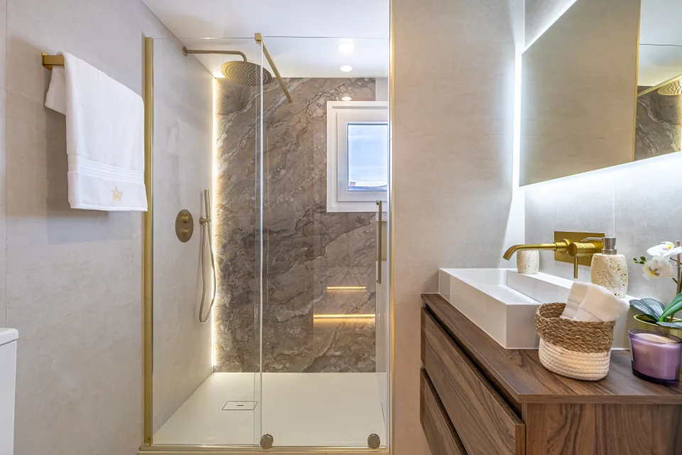 Interior design and architecture photograph of a modern bathroom with glass shower, golden fittings and wooden details in Cala de Mijas