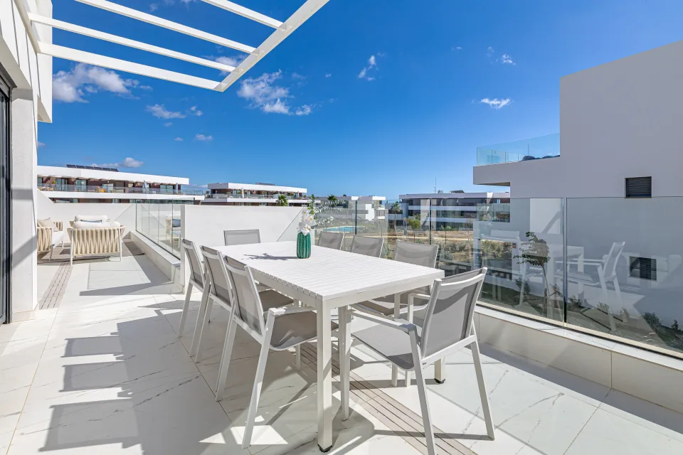 Fotografía de alquiler vacacional de una terraza moderna con mesa de comedor blanca y sillas cómodas bajo un cielo azul en Casares Costa