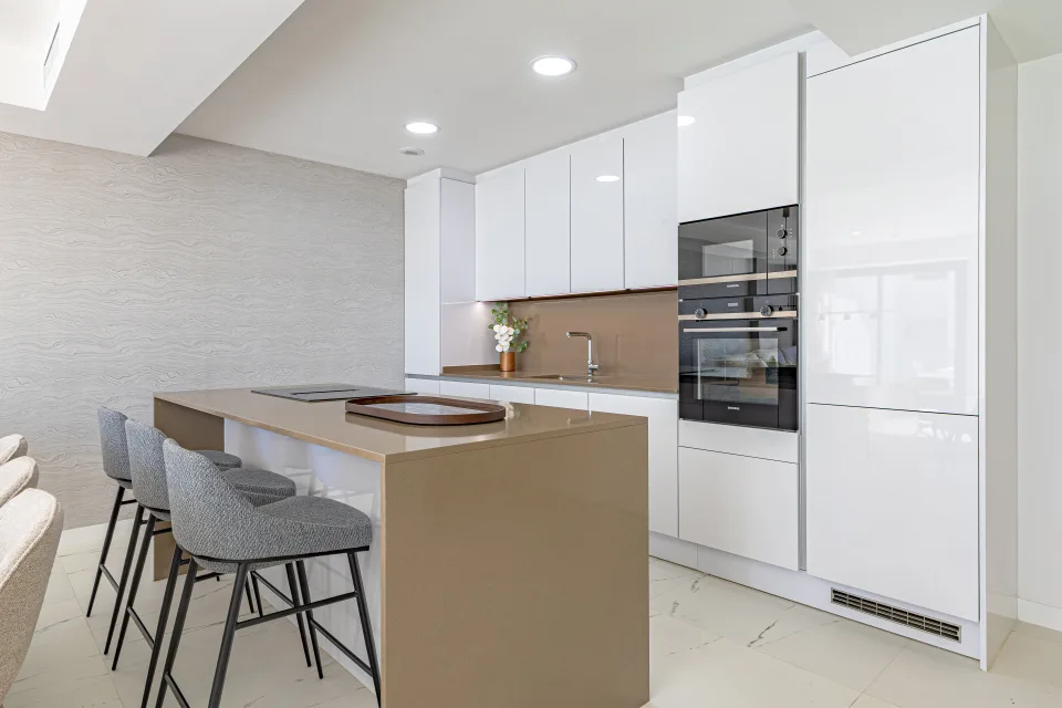 Fotografía de alquiler vacacional de una cocina moderna con superficies blancas, barra de desayuno y sillas de diseño en Casares Costa