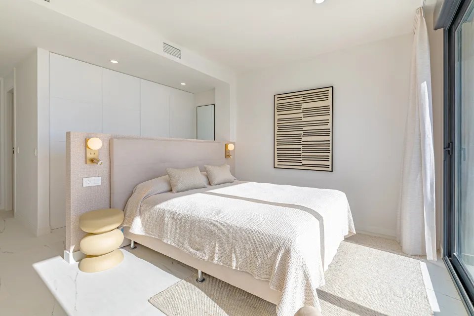Fotografía de alquiler vacacional de un dormitorio luminoso con cama grande, paredes claras y decoración minimalista en Casares Costa