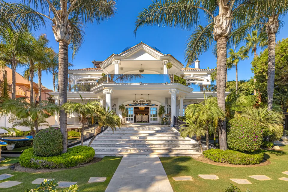 Fotografía de alquiler vacacional de una elegante villa con amplias terrazas, jardín cuidado y palmeras altas en Marbella