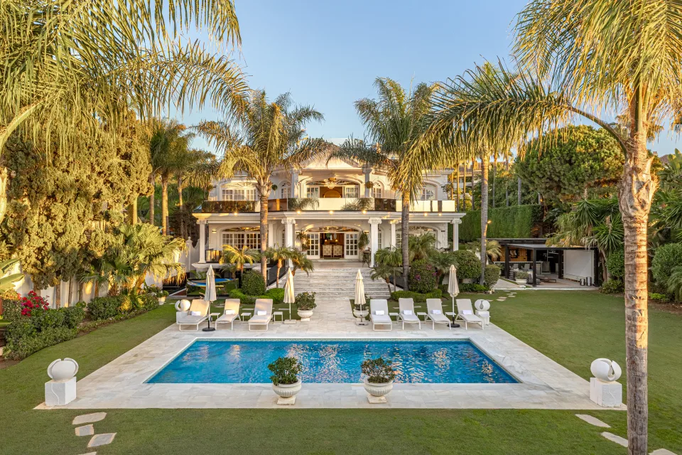 Fotografía de alquiler vacacional de una villa con piscina exterior rodeada de palmeras y tumbonas en Marbella