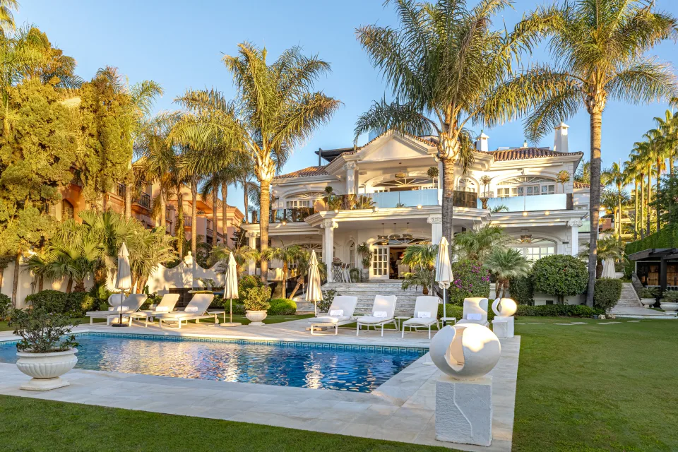 Fotografía de alquiler vacacional de un jardín con piscina, tumbonas blancas y palmeras alrededor en Marbella
