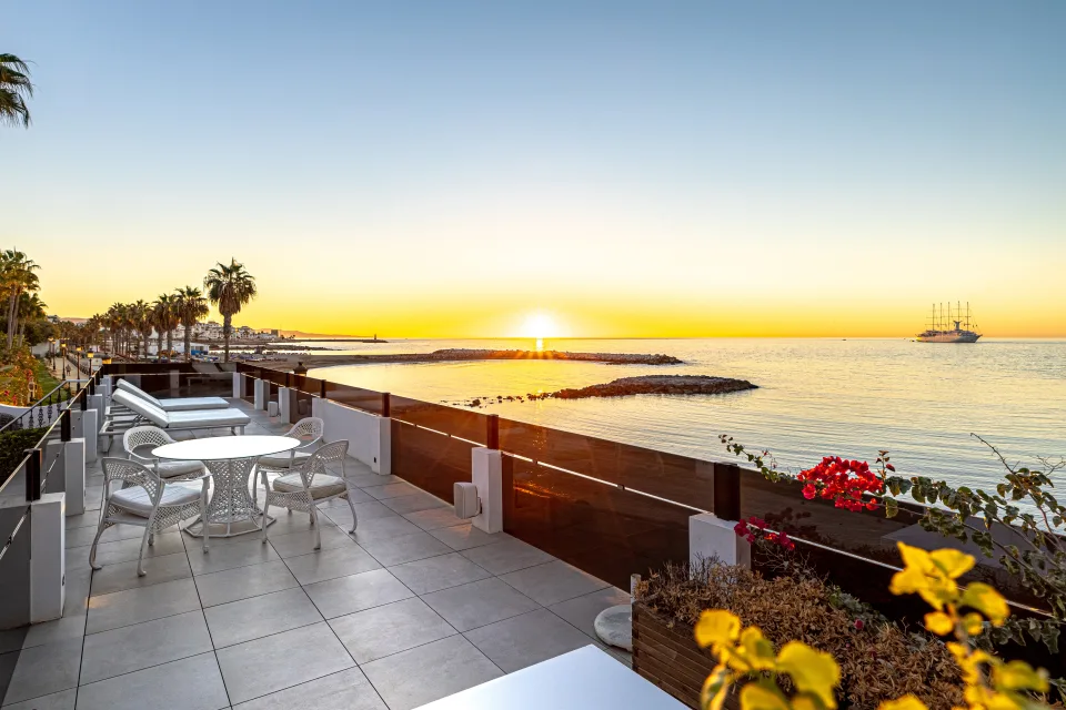 Fotografía de alquiler vacacional de una terraza con vistas al mar y al atardecer, mobiliario moderno y flores en primer plano en Marbella
