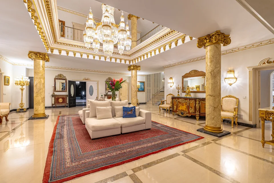 Fotografía de alquiler vacacional de un amplio vestíbulo con columnas doradas, chandelier elegante y sofá claro en Marbella