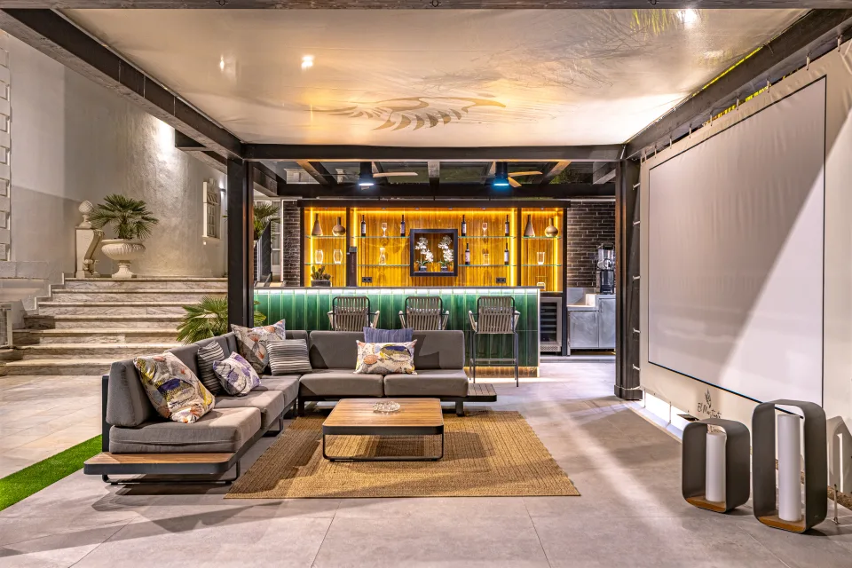 Fotografía de alquiler vacacional de un moderno salón exterior con sofá de diseño, barra de bar iluminada y grandes mesas de café en Marbella