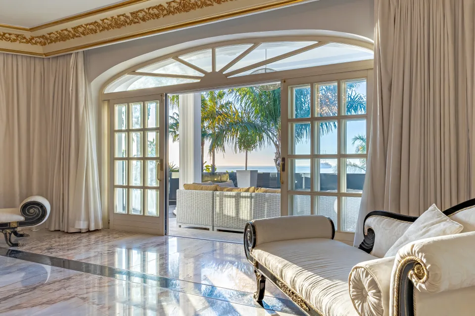 Fotografía de alquiler vacacional de un elegante salón con grandes ventanales, sofá claro y acceso a terraza con vistas al mar en Marbella
