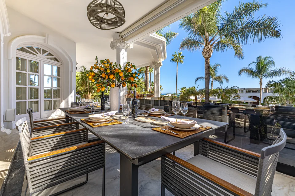 Fotografía de alquiler vacacional de un elegante comedor al aire libre con mesa oscura, sillas modernas y vistas de palmeras en Marbella