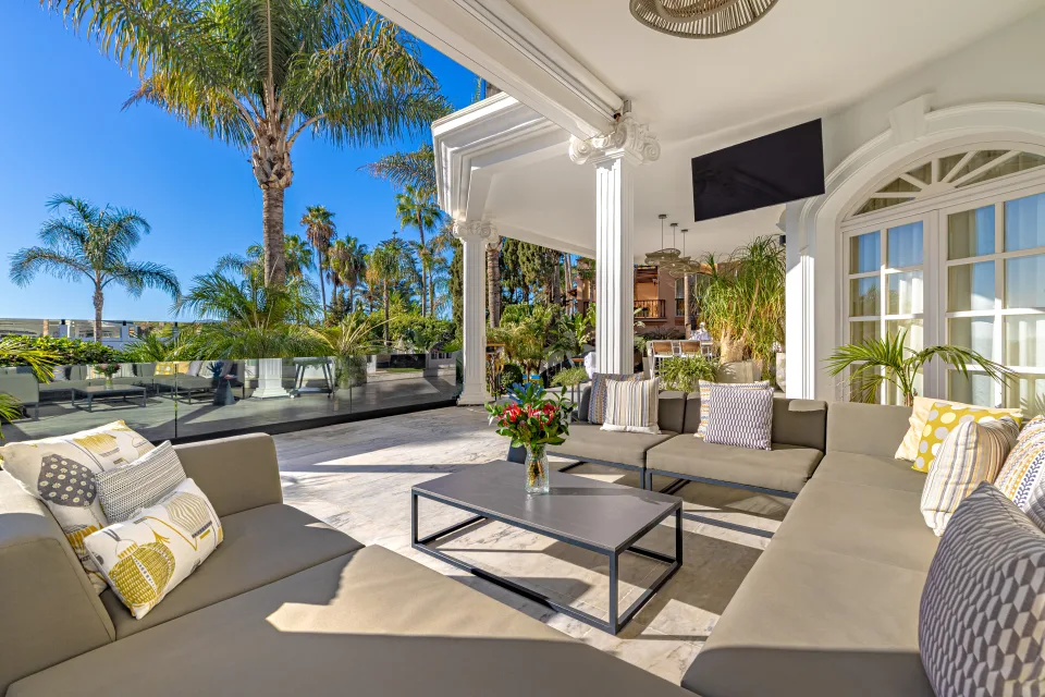 Fotografía de alquiler vacacional de un elegante salón exterior con sofás de diseño, mesa de centro y vistas a la palmera en Marbella