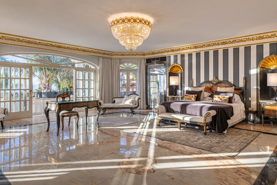 Fotografía de alquiler vacacional de un lujoso dormitorio con cama king size, lámpara de cristal y grandes ventanales en Marbella