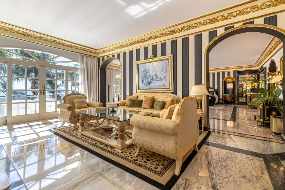 Fotografía de alquiler vacacional de un elegante salón con sofá en tonos crema, mesas de cristal y grandes ventanales con luz natural en Marbella