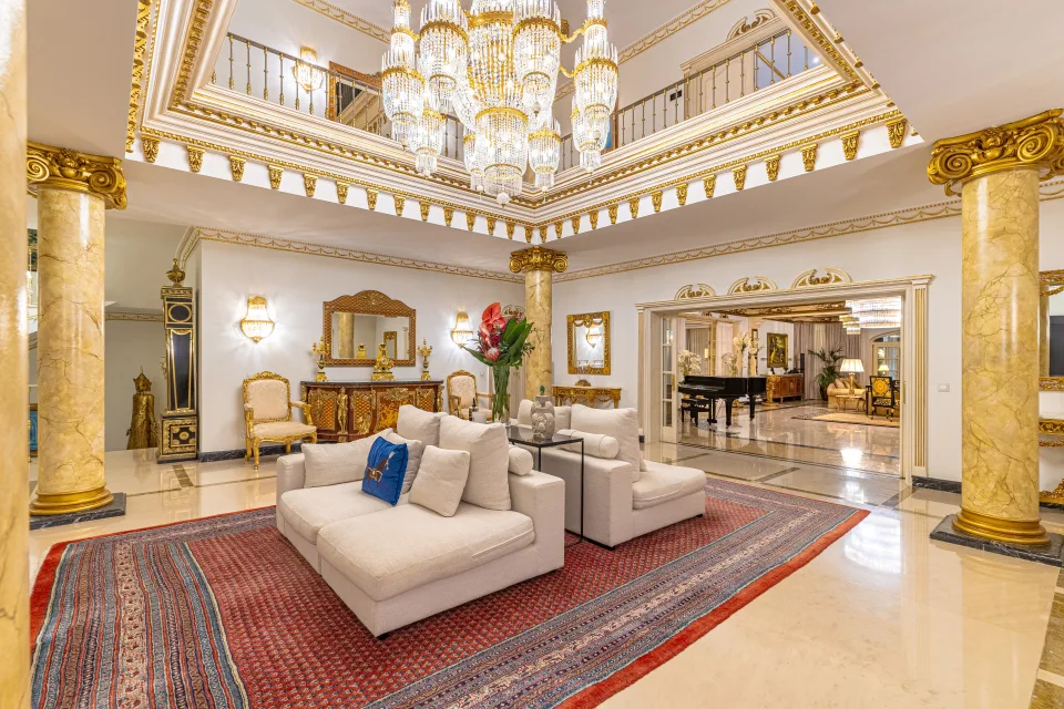 Fotografía de alquiler vacacional de un amplio vestíbulo con decoración lujosa, columnas doradas y una gran lámpara de cristal en Marbella
