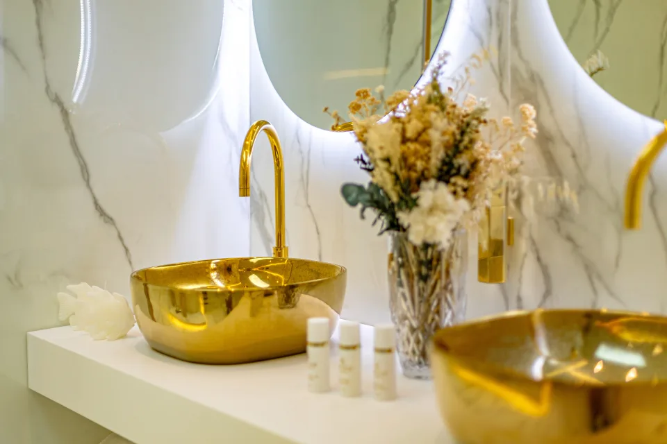 Fotografía de alquiler vacacional de un elegante lavabo dorado con grifería moderna y decoración floral en Marbella