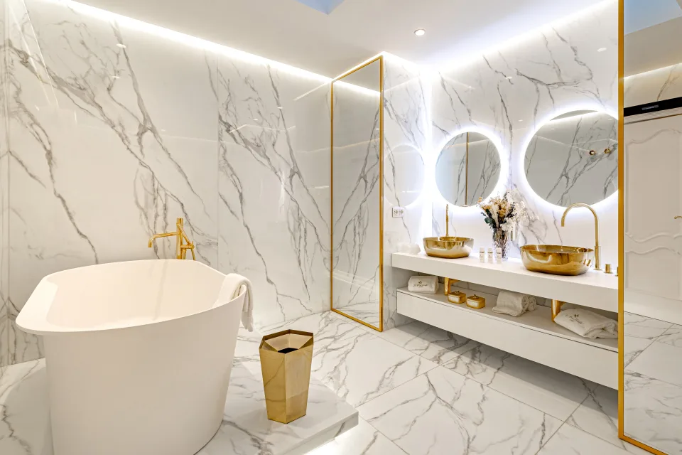 Fotografía de alquiler vacacional de un baño moderno con bañera independiente, espejos redondos iluminados y accesorios dorados en Marbella
