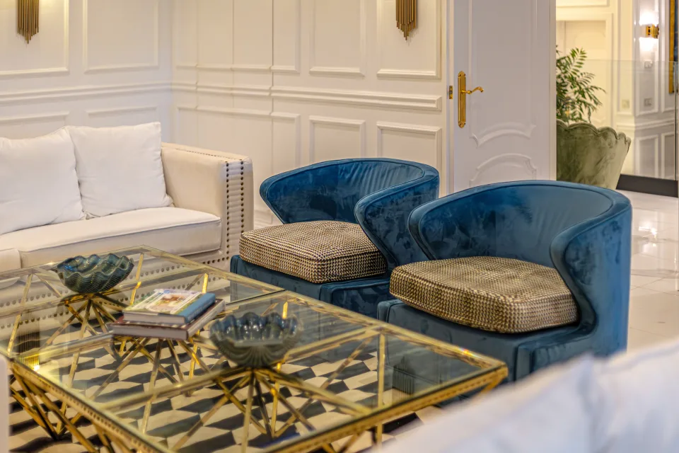 Fotografía de alquiler vacacional de un elegante salón con sofás blancos y sillas azules, mesas doradas y detalles decorativos en Marbella
