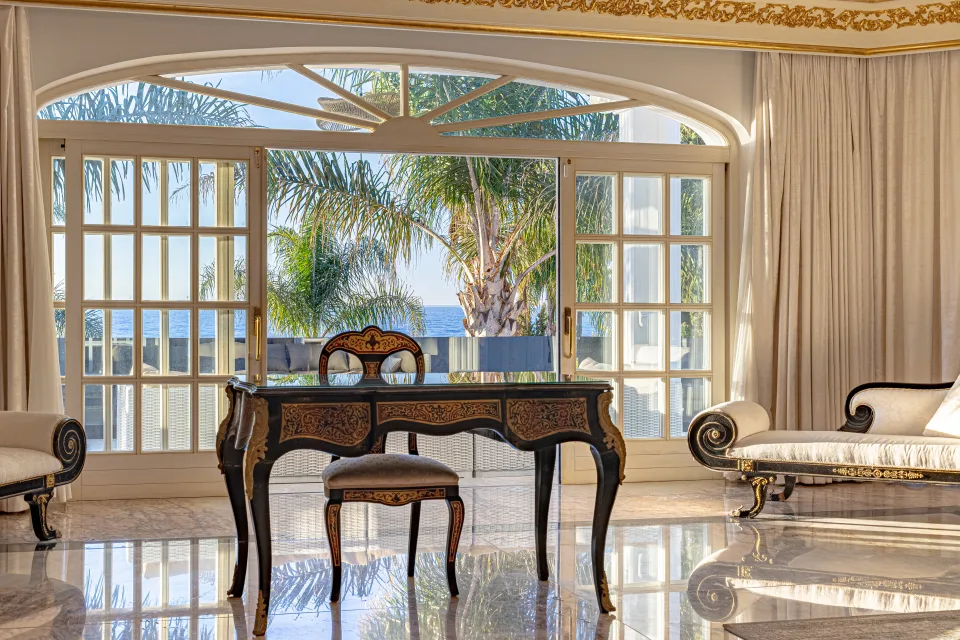 Fotografía de alquiler vacacional de un elegante salón con grandes ventanales, muebles de estilo clásico y vistas al mar en Marbella