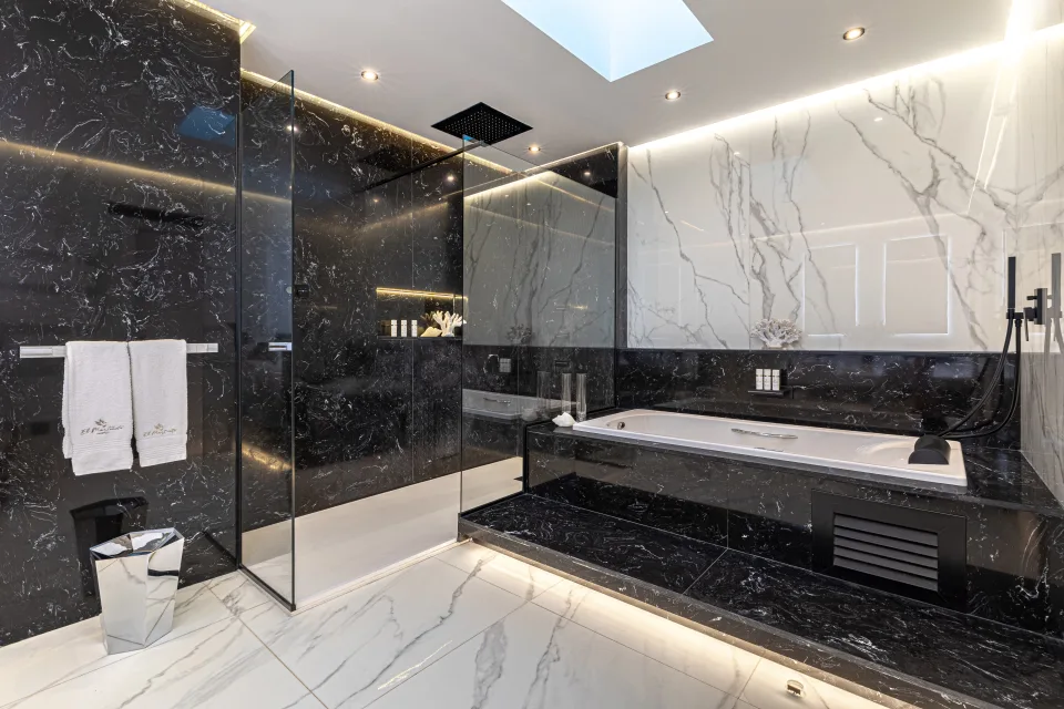 Fotografía de alquiler vacacional de un elegante baño con azulejos de mármol negro, ducha a ras de suelo y bañera empotrada en Marbella