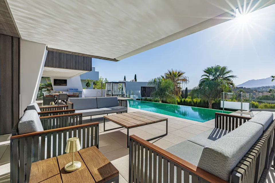 Fotografía de interiorismo y arquitectura de un exterior con terraza y piscina rodeada de vegetación y mobiliario moderno en Estepona