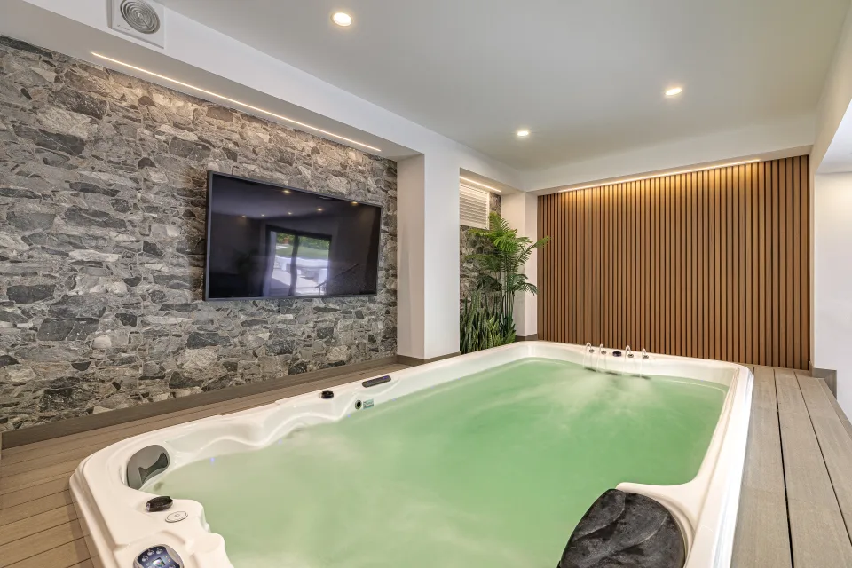 Fotografía de interiorismo y arquitectura de una zona de relajación con jacuzzi, pared de piedra natural y detalles en madera en Estepona