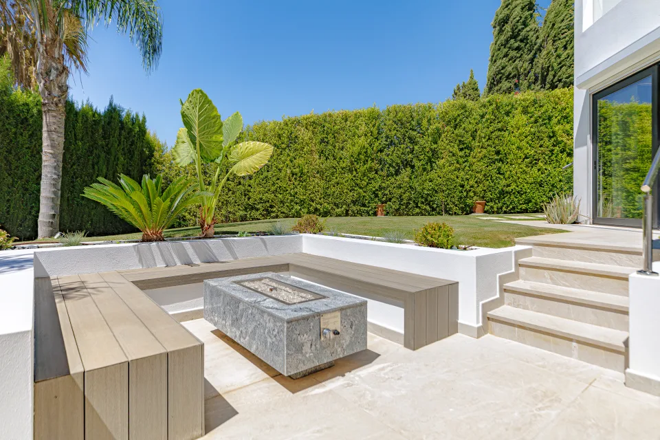 Fotografía de interiorismo y arquitectura de un exterior minimalista con zona de descanso, sofá de madera y fogón de piedra en Estepona