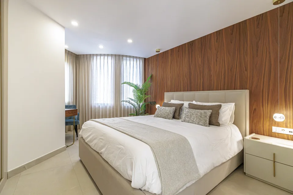 Fotografía de interiorismo y arquitectura de un dormitorio con pared de madera, iluminado por luz natural y con elegante mobiliario en Estepona