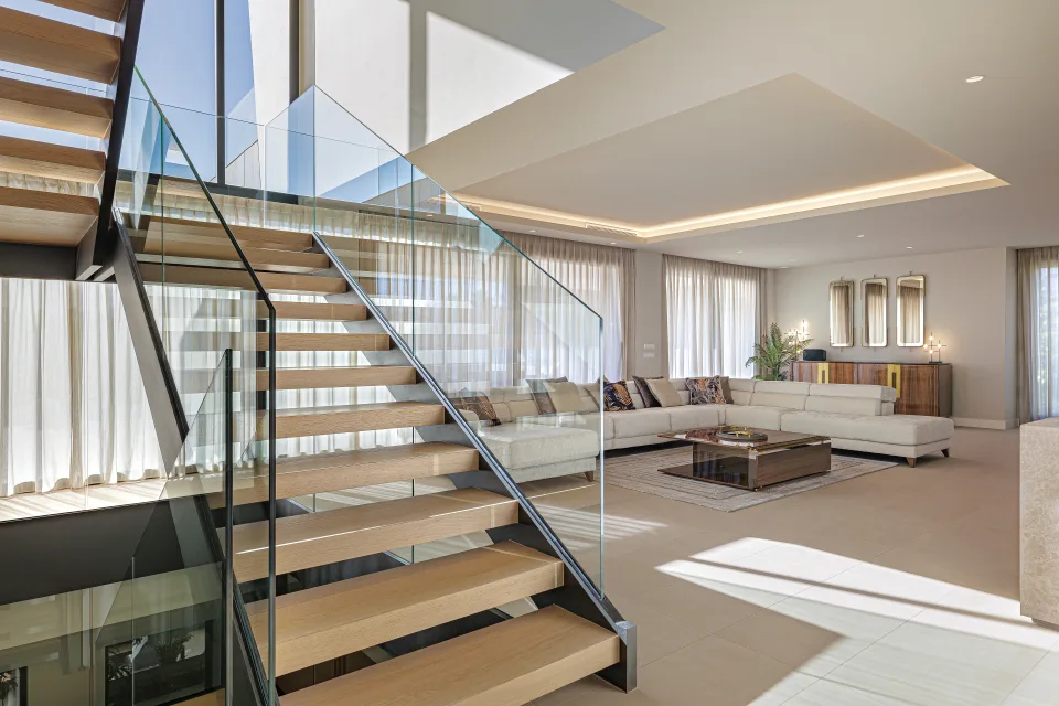 Interior design and architecture photograph of a spacious living room with large windows, wooden staircase and bright seating area in Estepona