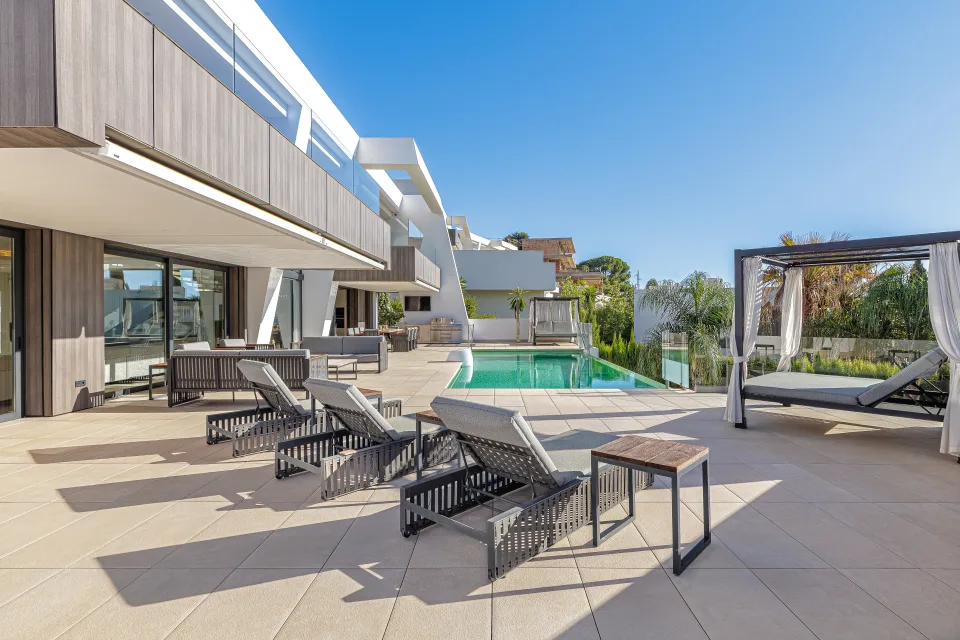 Interior design and architecture photograph of an outdoor area with a swimming pool, modern sun loungers and a stylish pergola in Estepona