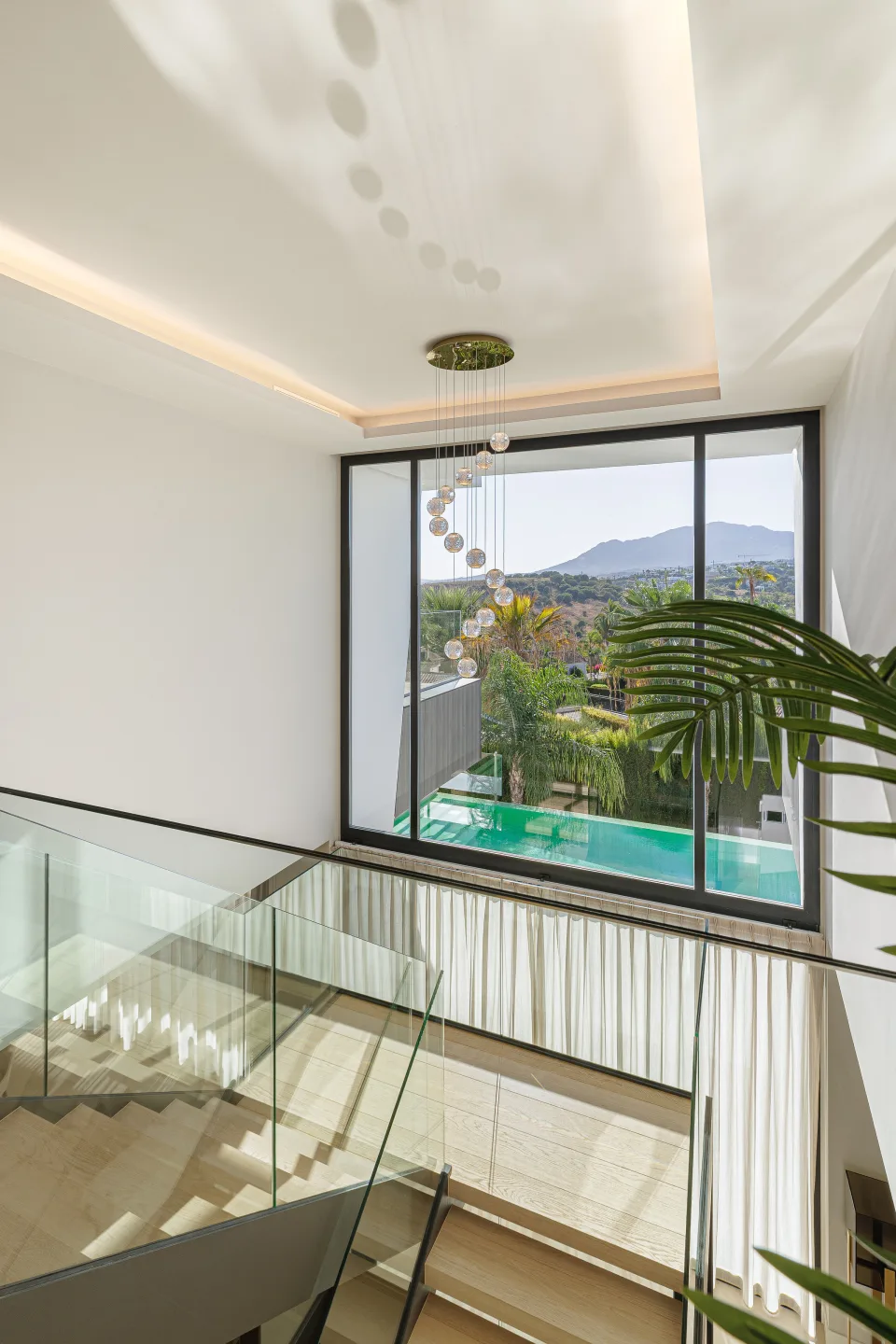 Interior design and architecture photograph of an elegant hallway with wooden stairs and a large window overlooking the pool in Estepona | 4M€ Villa in El Paraíso