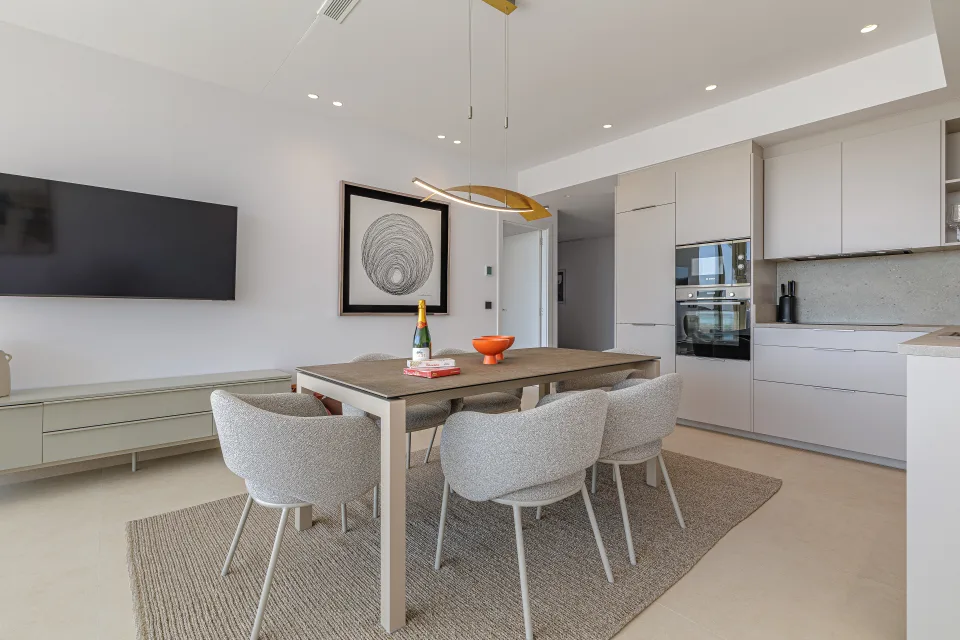 Vacation rental photograph of a modern dining area with a light wood table, upholstered neutral chairs and integrated kitchen in Benahavís