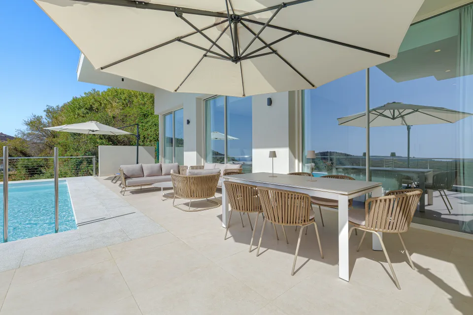 Fotografía de alquiler vacacional de un elegante porche con mesa comedor blanca, sillas de ratán y acceso a piscina en Benahavís