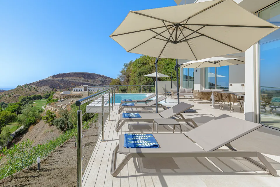 Fotografía de alquiler vacacional de una terraza con tumbonas, sombrillas y vistas panorámicas al paisaje en Benahavís