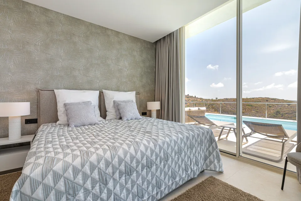 Fotografía de alquiler vacacional de un dormitorio luminoso con cama doble, vistas al exterior y decoración moderna en Benahavís