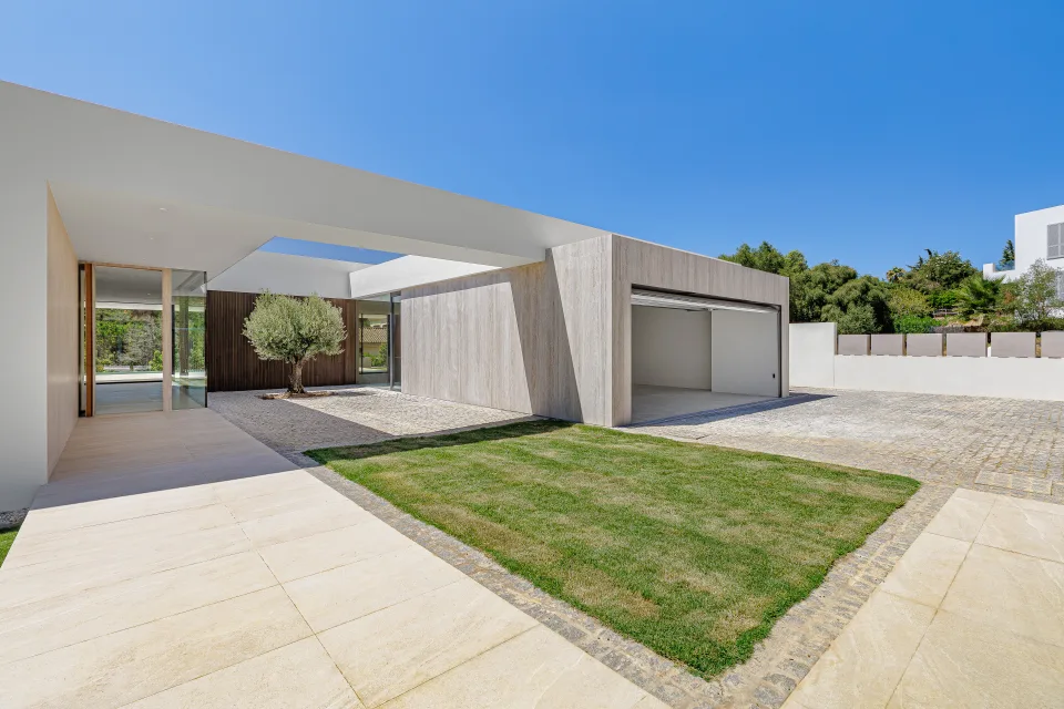 Fotografía de arquitectura de un patio con un olivo, paredes de piedra y luz natural iluminando el espacio en Sotogrande