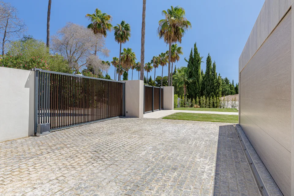 Fotografía de arquitectura de un acceso privado con puertas automáticas, rodeado de palmeras y vegetación en Sotogrande