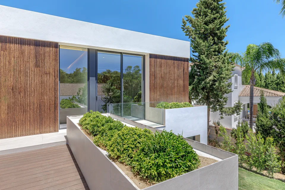 Fotografía de arquitectura de un acceso a terraza con barandilla de cristal, madera y jardines en la vegetación en Sotogrande