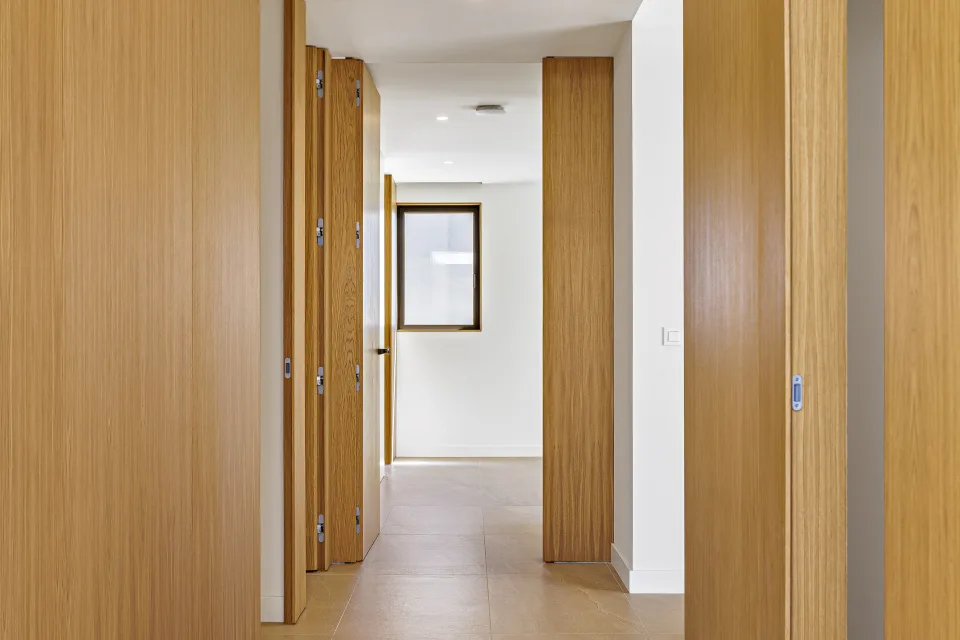 Fotografía de arquitectura de un pasillo luminoso con puertas de madera y suelos de cerámica clara en Sotogrande