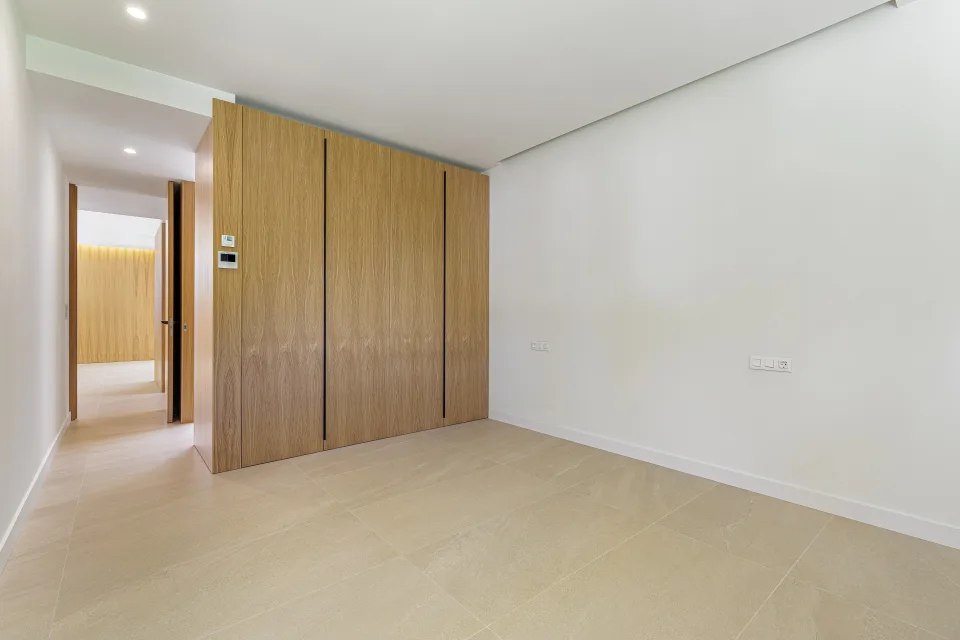 Fotografía de arquitectura de un dormitorio con paredes claras, suelo de piedra y armario empotrado de madera en Sotogrande