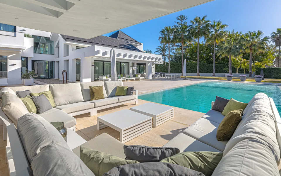 Interior design and architecture photograph of an elegant outdoor lounge with light sofas, low tables and a pool in the garden in Guadalmina Baja