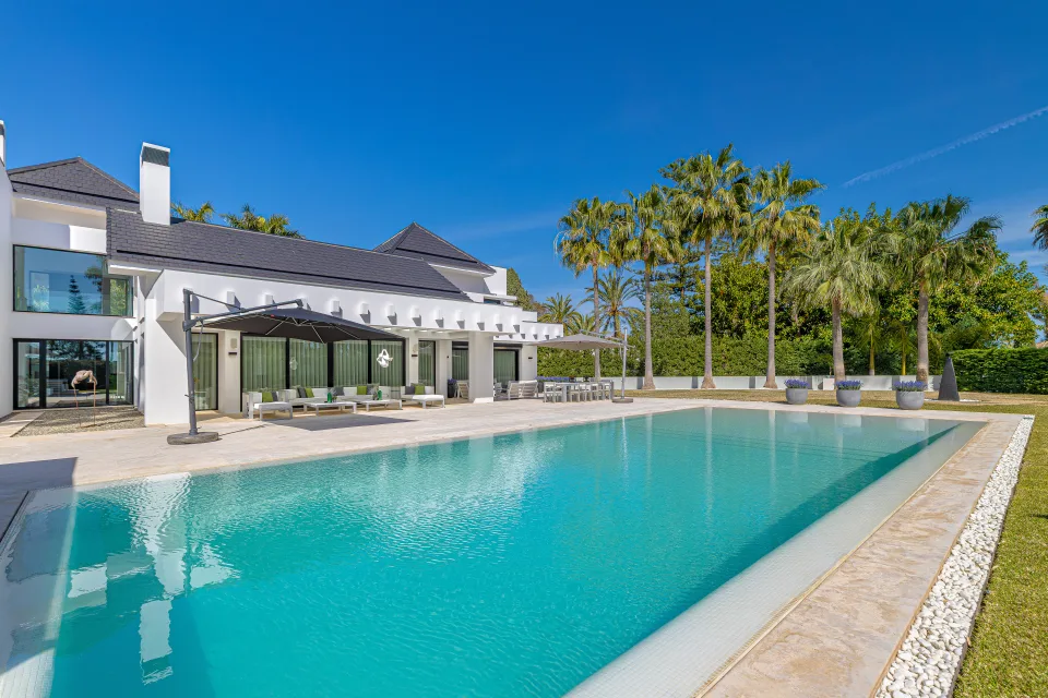 Fotografía de interiorismo y arquitectura de una villa con piscina desbordante rodeada de palmeras y amplias terrazas en Guadalmina Baja