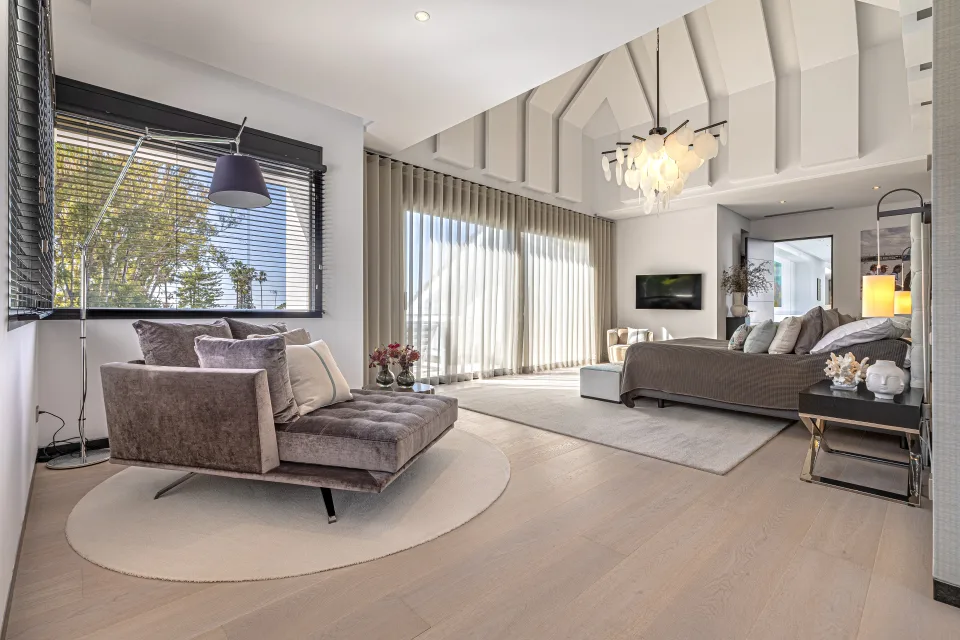 Fotografía de interiorismo y arquitectura de un amplio dormitorio con grandes ventanales, cama elegante y mobiliario moderno en Guadalmina Baja