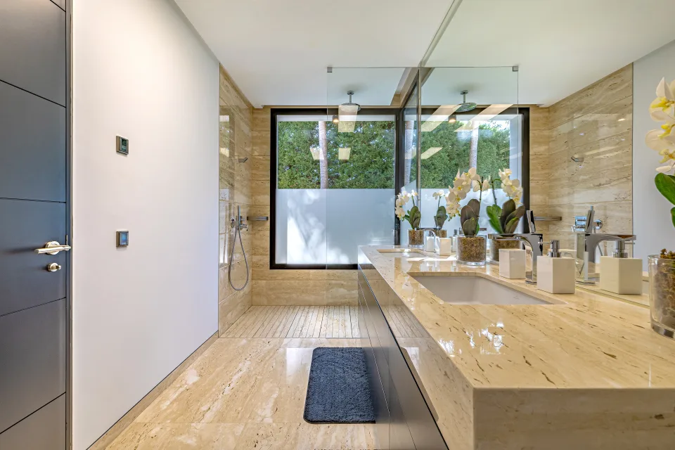 Fotografía de interiorismo y arquitectura de un moderno baño con paredes de piedra clara, amplia encimera de mármol en Guadalmina Baja