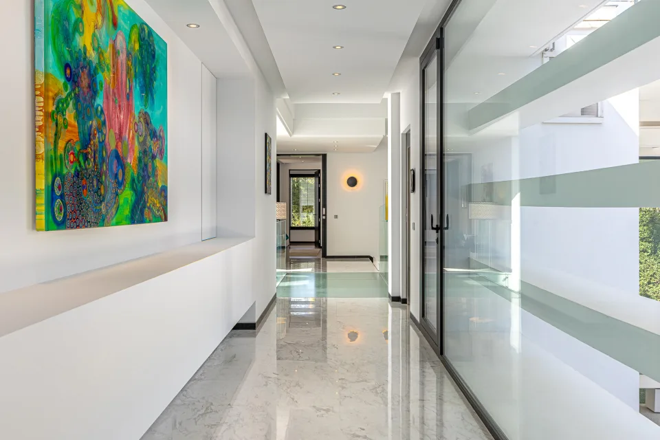 Fotografía de interiorismo y arquitectura de un luminoso pasillo con suelos de mármol y obras de arte en las paredes en Guadalmina Baja